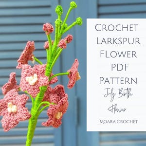 May include: A crochet larkspur flower with pink petals and a white center, on a green stem. The image includes text that reads "CROCHET LARKSPUR FLOWER PDF PATTERN July Birth Flower MOARA CROCHET."