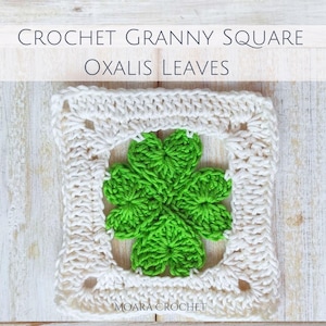 Könnte beinhalten: Ein weißes Häkel-Oma-Quadrat mit einem grünen vierblättrigen Kleeblatt-Design in der Mitte. Das Quadrat befindet sich auf einem weißen Holzgrund. Der Text "CROCHET GRANNY SQUARE OXALIS LEAVES" befindet sich über dem Quadrat. Der Text "MOARA CROCHET" befindet sich unter dem Quadrat.