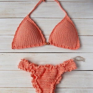 Pu&ograve; includere: Un bikini in crochet color corallo. La parte superiore &egrave; di stile triangolare con chiusura a nodo sul collo e sulla schiena. La parte inferiore ha un bordo con volant.