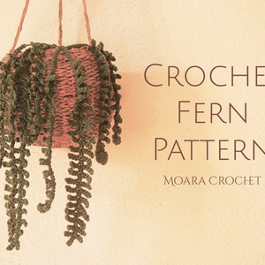 May include: A crocheted fern plant hanging from a brown woven basket. The text "CROCHET FERN PATTERN MOARA CROCHET" is written below the plant.