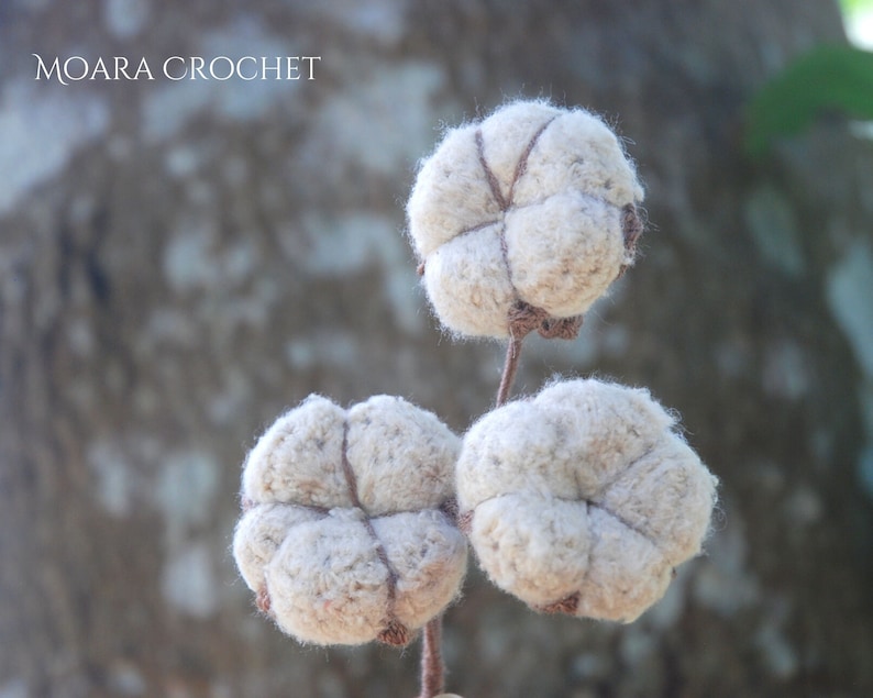 May include: Three white crocheted cotton boll ornaments with brown yarn accents. The bolls are arranged on a stem.