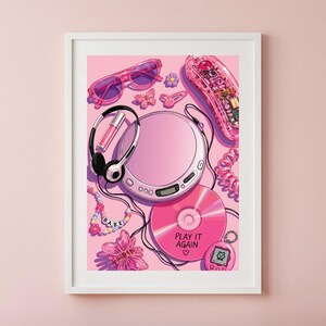 May include: A framed art print featuring a pink aesthetic collage of a portable CD player, headphones, a translucent pink corded telephone, a pink CD labeled PLAY IT AGAIN, pink sunglasses, a beaded necklace with the word BABE, and a digital pet.