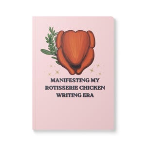 May include: A light pink notebook featuring a central illustration of a roasted rotisserie chicken with a sprig of green herbs. Below the chicken, the text reads: MANIFESTING MY ROTISSERIE CHICKEN WRITING ERA, accented by small gold star icons.