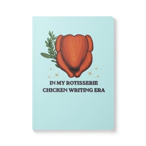 May include: A light blue notebook featuring a central illustration of a roasted rotisserie chicken with a sprig of green rosemary. Below the chicken, the text reads IN MY ROTISSERIE CHICKEN WRITING ERA, accented by small gold star-shaped sparkles.