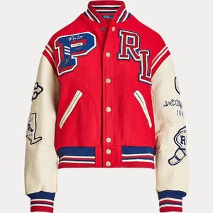 Pode incluir: Um casaco estilo universitário vermelho com mangas cor de creme, apresentando uma letra P azul e branca no peito direito e uma letra RL no esquerdo. O casaco tem punhos e bainha canelados às riscas, fecho de botões de pressão e vários emblemas.