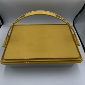 May include: A rectangular storage container with a solid yellow lid and a matching yellow arched handle. The base of the container is white, and the lid features a smooth, flat surface with a raised border. The handle is attached to the sides.