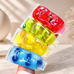 May include: Four clear squeeze tubes labeled Chiboki, each filled with a different colored gel and small decorative shapes. The tubes contain red gel with strawberries, green gel with bear shapes, yellow gel with lemon slices, and blue gel with blueberries.