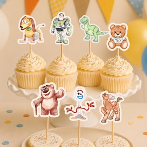 Può includere: Un set di decorazioni per cupcake e biscotti con personaggi illustrati tra cui un cane, un ranger spaziale, un dinosauro verde, un orsacchiotto con la parola TOY, un orso rosa, un personaggio forchetta e un cavallo, fissati su bastoncini di legno.