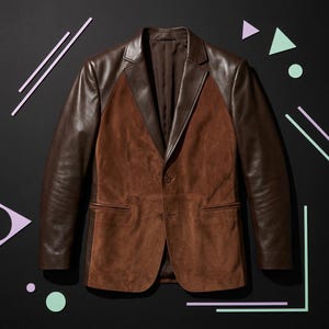May include: A brown blazer featuring a combination of smooth leather sleeves and lapels with a textured suede front panel. The garment includes two front buttons, notched lapels, and two horizontal welt pockets on the lower front section.