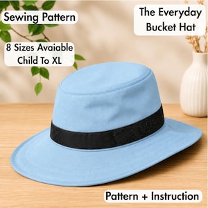 May include: A light blue bucket hat with a black band featuring a subtle floral embroidery pattern. Text on the image reads: Sewing Pattern, The Everyday Bucket Hat, 8 Sizes Available Child To XL, and Pattern + Instruction.