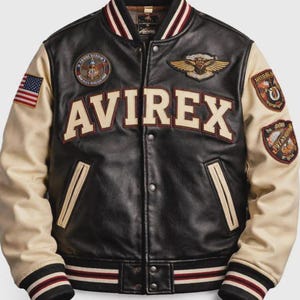 May include: A black leather varsity jacket with cream-colored sleeves, featuring the word AVIREX in large cream letters across the chest. The jacket includes multiple embroidered patches, a striped ribbed collar, cuffs, and hem, and snap buttons.