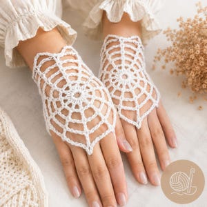 May include: A pair of white fingerless gloves featuring an intricate, circular spiderweb crochet pattern. The gloves are crafted from fine white yarn, with a delicate openwork design that radiates from a central point across the back of the hand.