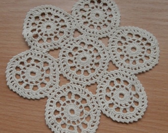 May include: A white crocheted doily with a flower design. The doily is made up of seven circles connected together.