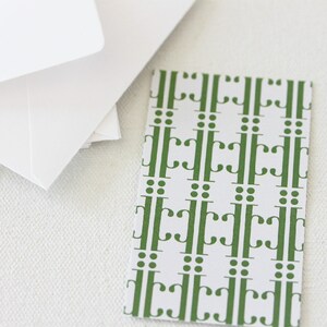 May include: A white card with a green repeating pattern of stylized letters and dots.