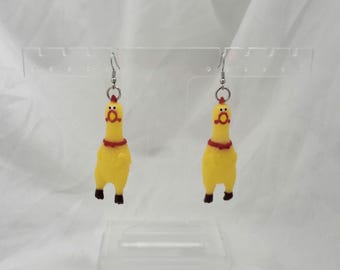 May include: A pair of drop earrings featuring miniature yellow rubber chickens with red collars and open beaks. The chickens are suspended from silver-toned metal earring hooks, creating a playful and distinct accessory for ears.