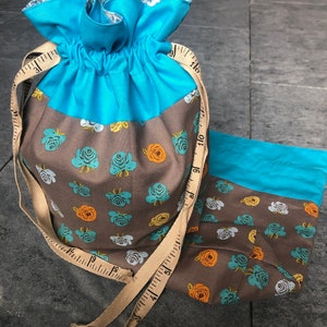 Könnte beinhalten: Zwei Kordelzugbeutel. Der größere Beutel ist türkis und braun mit einem Blumenmuster. Ein beiges Maßband ist um die Tasche gewickelt. Der kleinere Beutel ist türkis und braun mit einem Blumenmuster.
