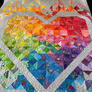 May include: A colorful quilt featuring a large heart design. The heart is composed of various fabric pieces in a rainbow of colors, including red, orange, yellow, green, blue, and purple. The quilt has a gray background and a geometric pattern.