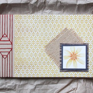 Puede incluir: Tarjeta rectangular hecha a mano con un estampado floral amarillo y un acento de arpillera. La tarjeta presenta un diseño cosido en rojo en el lado izquierdo y una imagen de flor enmarcada. La combinación de colores es amarilla, marrón y roja.