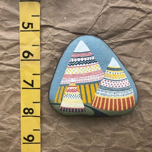 Puede incluir: Pintura de roca pintada a mano que representa tres tipis coloridos con patrones geom&eacute;tricos en tonos rojos, amarillos, blancos y negros. Los tipis est&aacute;n pintados sobre un fondo gris.