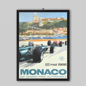 May include: A framed vintage-style poster depicting two race cars on a track in Monaco. The scene features a coastal town and a castle in the background. Text includes 22 mai 1966, MONACO, and 24e GRAND PRIX AUTOMOBILE in blue and black lettering.