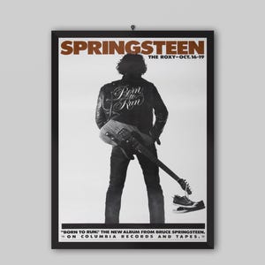 May include: A framed poster featuring a black and white image of a person from behind, wearing a leather jacket with the text Born to Run, holding a guitar. The text Springsteen, The Roxy-Oct. 16-19, and Born to Run: The New Album from Bruce Springsteen on Columbia Records and Tapes is visible.