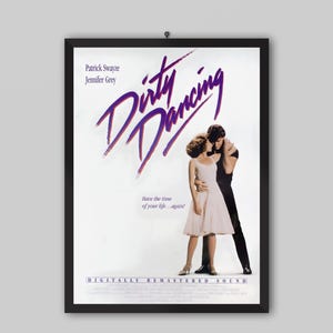 May include: A framed film poster for Dirty Dancing featuring Patrick Swayze and Jennifer Grey. The poster has a white background with purple text, a central image of two people dancing, and the tagline Have the time of your life...again!