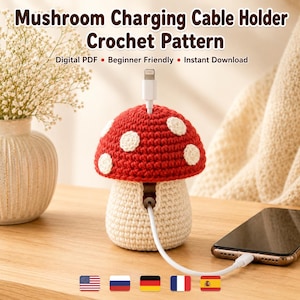 May include: A crochet mushroom charging cable holder with a red cap featuring white spots and a cream-colored stem. The text reads: Mushroom Charging Cable Holder Crochet Pattern, Digital PDF, Beginner Friendly, Instant Download.