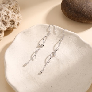 May include: A pair of silver-toned dangle earrings featuring a delicate spiral metal design. Each earring consists of a thin, twisted metallic strand accented with small, round beads at the ends, suspended from a simple curved hook wire.