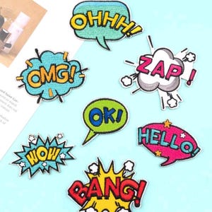 May include: Eight colorful embroidered iron-on patches with different words in speech bubbles. The words are "OHHH!", "OMG!", "ZAP!", "OK!", "WOW", "HELLO!", "BANG!" and "HELLO!"