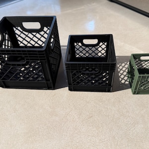 May include: Three rectangular storage crates with a lattice grid pattern and integrated handles. The two larger crates are black, while the smallest crate is olive green. Each crate features an open top and a hollow interior structure.