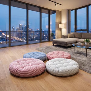 May include: Four round floor cushions arranged on a wooden floor. The cushions feature tufted surfaces and striped patterns in blue and white, red and white, and grey and white. Each cushion is circular with a thick, soft, padded construction.