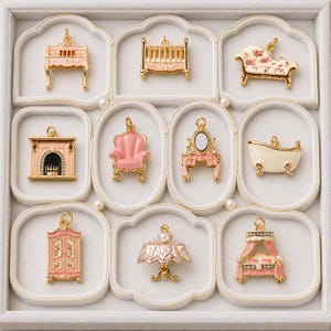 Può includere: Una collezione di nove ciondoli in metallo dorato a forma di mobili in miniatura, tra cui un letto, una culla, una chaise longue, un camino, una poltrona, una toeletta, una vasca da bagno, un armadio e un tavolo, con dettagli in smalto rosa e bianco.