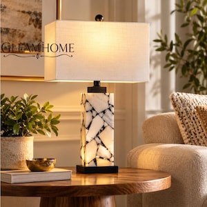 May include: A table lamp with a rectangular white fabric shade and a square base constructed from white marble pieces with black veining. The lamp features a black metal finial and base, with the text GLEAMHOME printed on the shade.