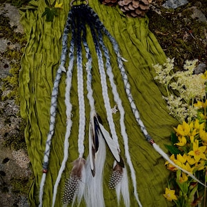 May include: A set of synthetic dreadlocks featuring a color gradient from dark navy blue at the top to white at the ends. The strands are adorned with small silver-toned charms, including a star, and are accented with natural-looking feathers.