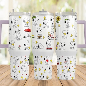 May include: A white stainless steel tumbler with a handle, featuring a repeating pattern of Snoopy and Woodstock in various activities. The design includes small colourful accents like a red umbrella, a red skateboard, a yellow sunflower, and red hearts.