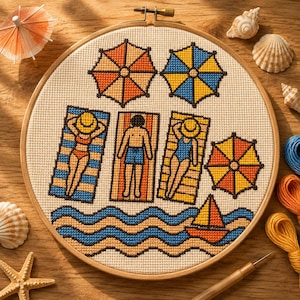 Può includere: Un telaio da ricamo circolare in legno contenente un disegno a punto croce di una scena in spiaggia. Il motivo presenta tre figure sdraiate su asciugamani a righe, tre ombrelloni colorati, una piccola barca a vela e onde stilizzate.