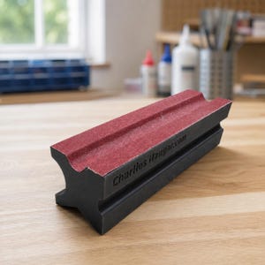 May include: A black sanding block with a cross-shaped profile and a red abrasive surface on the top side. The side of the block features the embossed text CharliesHangar.com. The tool has a rigid construction with a concave top section.
