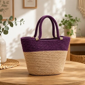 May include: A two-toned crochet handbag featuring a deep purple upper section and a light beige lower section. The bag has two matching purple crochet handles attached to the body with gold-toned metal hardware, creating a structured open-top design.