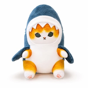 May include: A plush toy featuring an orange and white tabby cat wearing a dark blue shark costume. The cat has large black eyes, a small pink nose, and a white belly. The shark hood has white felt teeth, and the cat's paws show pink paw pads.