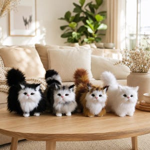 May include: Four plush cat figurines with long, fluffy fur arranged in a row on a wooden table. The cats feature distinct color patterns: one black and white, one grey and white, one brown and white, and one solid white, all with pink noses.