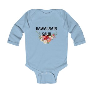 Peut inclure: Un body à manches longues bleu clair avec le texte noir KAWALNAIN KAUR centré sur la poitrine. Sous le texte se trouve un arrangement floral coloré composé de fleurs rouges, roses, orange et blanches avec des feuilles et des tiges vertes.