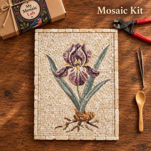 Op de afbeelding: Een mozaïekset met een rechthoekig stenen paneel met een paarse irisbloem met groene bladeren en wortels. De set bevat een kartonnen doos met het label My Mosaic Lab, een tang met rode handgrepen, een metalen pincet en een houten lepel.