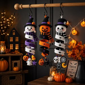 Puede incluir: Tres decoraciones de ganchillo colgantes que representan un fantasma, una calabaza y un esqueleto, cada uno con sombrero y bufanda. Las figuras están unidas a colas en espiral adornadas con pequeños dijes como calabazas y estrellas.