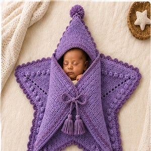 Puede incluir: Una manta de arrullo para bebé tejida a ganchillo en color violeta con forma de estrella, que incluye una capucha con un pompón, un patrón de punto texturizado y un cierre central de lazo con dos borlas decorativas para envolver al bebé.