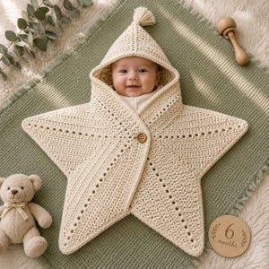 May include: A cream-colored crocheted star-shaped baby swaddle blanket with a pointed hood and a single wooden button closure. The swaddle features an openwork stitch pattern along the star points and a small tassel at the top of the hood.