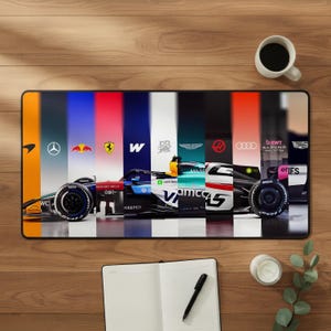 May include: A rectangular desk mat featuring a composite design of Formula 1 race cars and team logos arranged in vertical color-blocked panels. The graphic includes various automotive branding elements and racing car silhouettes across the surface.