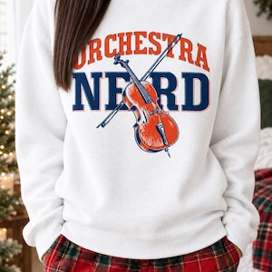 Könnte beinhalten: Ein weißes langärmeliges Sweatshirt mit Rundhalsausschnitt, das den orangefarbenen Schriftzug ORCHESTRA und den dunkelblauen Schriftzug NERD zeigt. Eine Grafik eines orangefarbenen Cellos mit dunkelblauem Bogen liegt mittig.