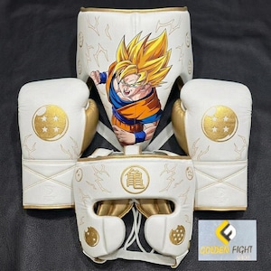 May include: A white boxing set featuring two gloves and two headguards with gold accents. The gear displays a graphic of a spiky-haired character in an orange gi, gold dragon ball symbols with four stars, and a circular emblem with Japanese kanji text.