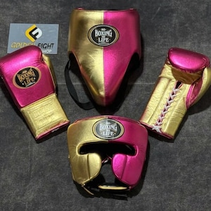 Op de afbeelding: Een boksset bestaande uit twee metallic roze en gouden bokshandschoenen, een hoofdbeschermer en een tok. Elk item heeft een zwart ovaal embleem met de tekst NO BOXING NO LIFE. Een klein bordje toont de tekst GOLDEN FIGHT SHOP.