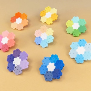 May include: Seven flower-shaped ornaments crafted from small, circular plastic beads. Each ornament features a white center surrounded by six petals in varying shades of orange, yellow, green, light blue, dark blue, purple, and pink-red gradients.